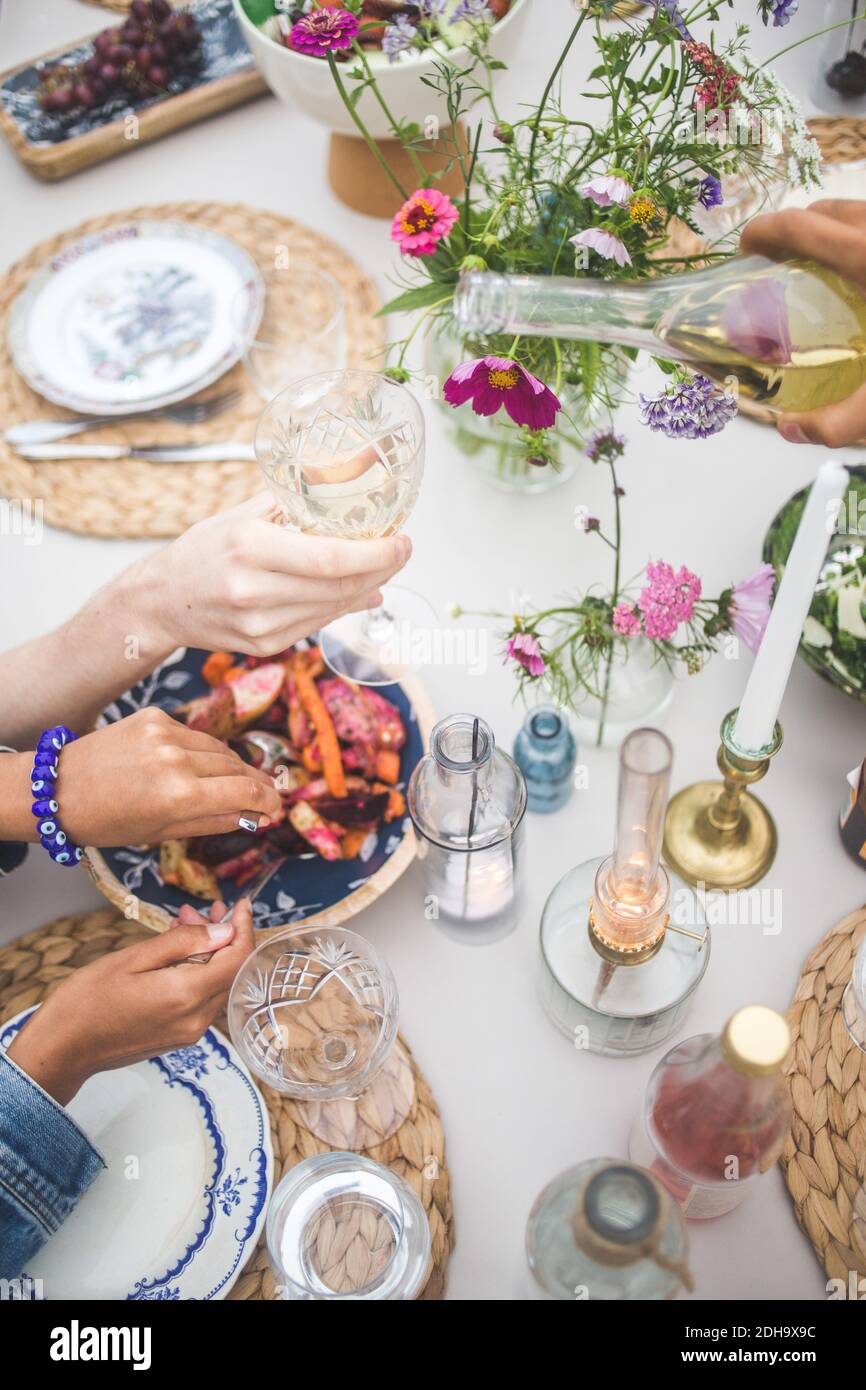 High-Angle-Ansicht von beschnitten Hand Gießen Wein während Frau Serviert Speisen bei geselligen Treffen auf der Terrasse Stockfoto