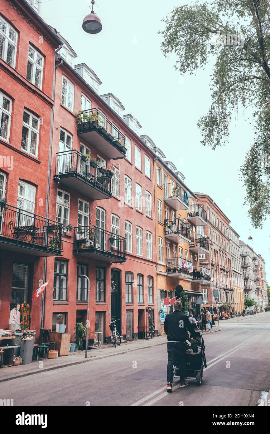 Rückansicht des Mannes, der den Kinderwagen auf die Straße schiebt Gebäude in der Stadt Stockfoto