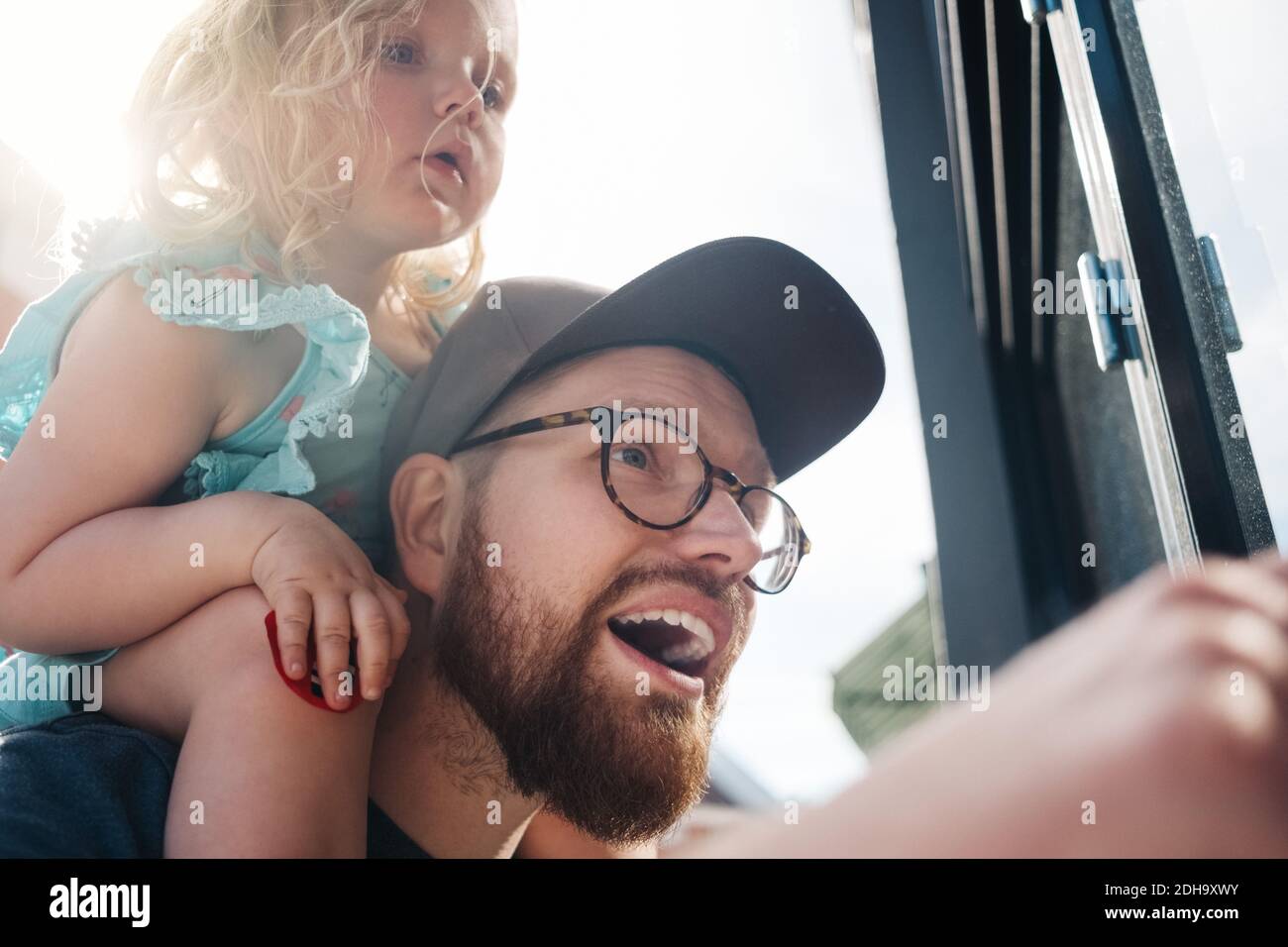 Low-Angle-Ansicht des Vaters reden, während die Tochter auf Schultern an sonnigen Tagen Stockfoto