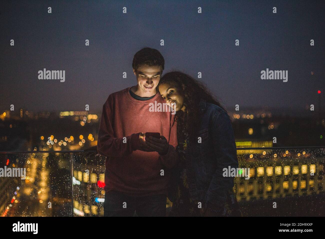 Junger Mann zeigt Smartphone zu weiblichen Freund während der sozialen Nächtliche Zusammenkunft auf der Terrasse Stockfoto