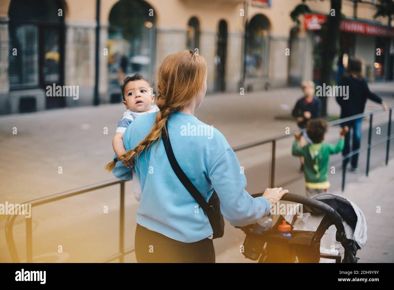 Rückansicht der Mutter, die mit Söhnen geht, während sie das Baby schiebt Kinderwagen auf dem Bürgersteig in der Stadt Stockfoto