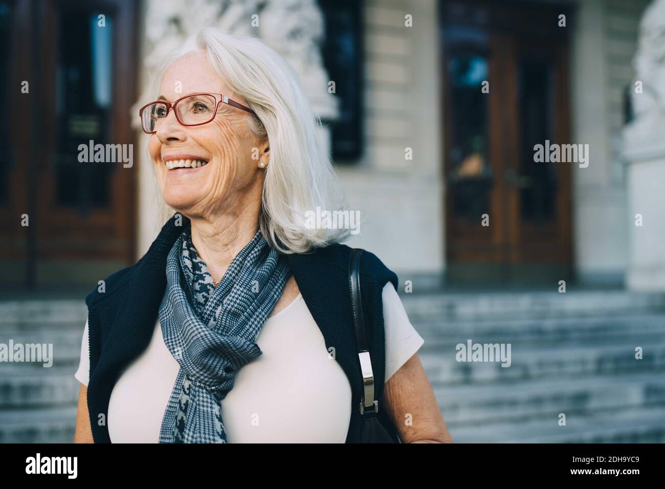 Lächelnde ältere Frau schaut weg, während sie die Stadt erkundet Stockfoto