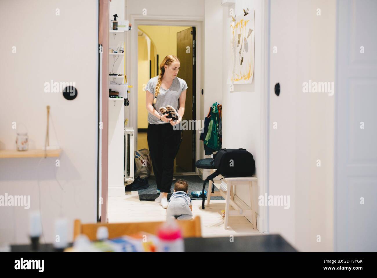 Mutter hält Schuhe und Kleinkind kriecht auf dem Boden zu Hause Stockfoto