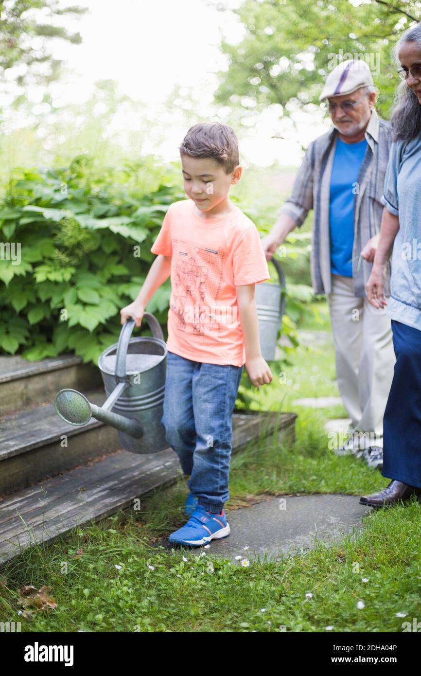 Junge trägt Gießkanne mit Großeltern zu Fuß im Hinterhof Stockfoto