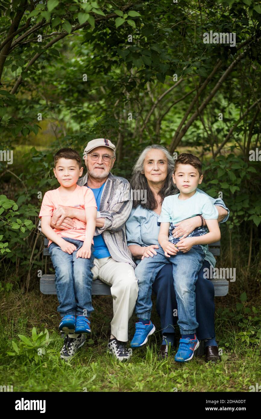 Porträt von Großeltern sitzen mit Zwillingsgroßeltern auf Bank gegen Pflanzen im Hinterhof Stockfoto