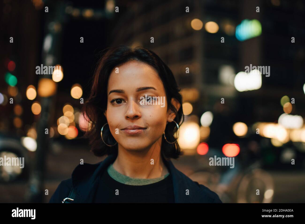 Porträt einer lächelnden Frau, die nachts in einer beleuchteten Stadt steht Stockfoto