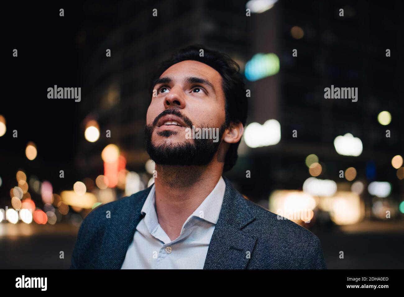 Betrachtender Mann, der aufschaut, während er nachts in der Stadt steht Stockfoto
