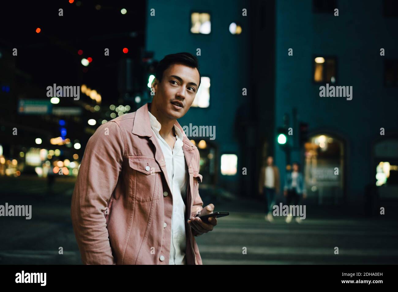 Betrachten junger Mann mit Telefon wegschauen, während im Stehen Beleuchtete Stadt bei Nacht Stockfoto