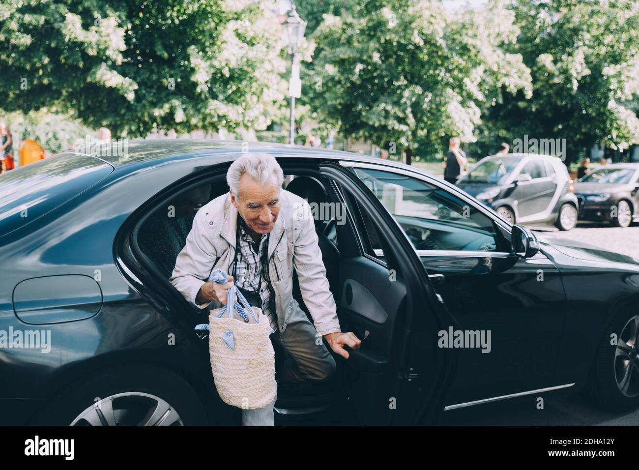 Senior Mann hält Tasche aus schwarzen Auto in Stadt Stockfoto