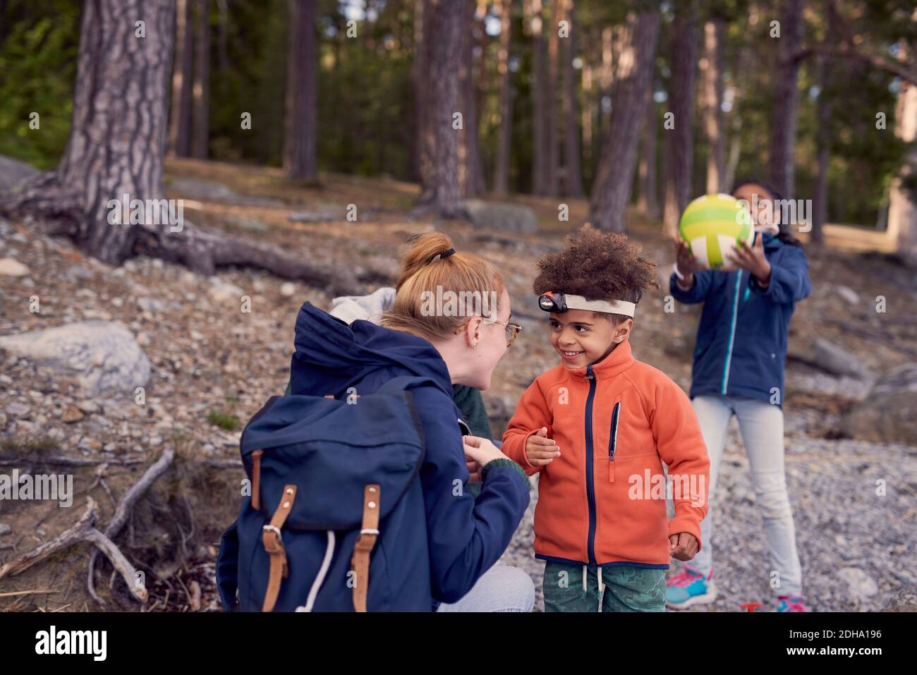 Mutter sieht lächelnden Jungen mit Stirnlampe, während Tochter spielt Mit Fußball im Hintergrund Stockfoto