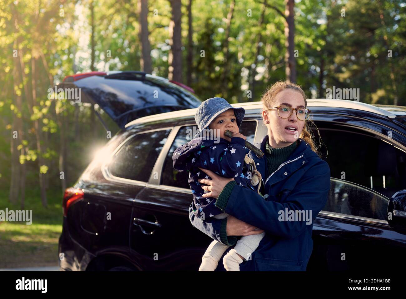 Junge Frau mit Baby Junge, während sie gegen Auto in Wald Stockfoto