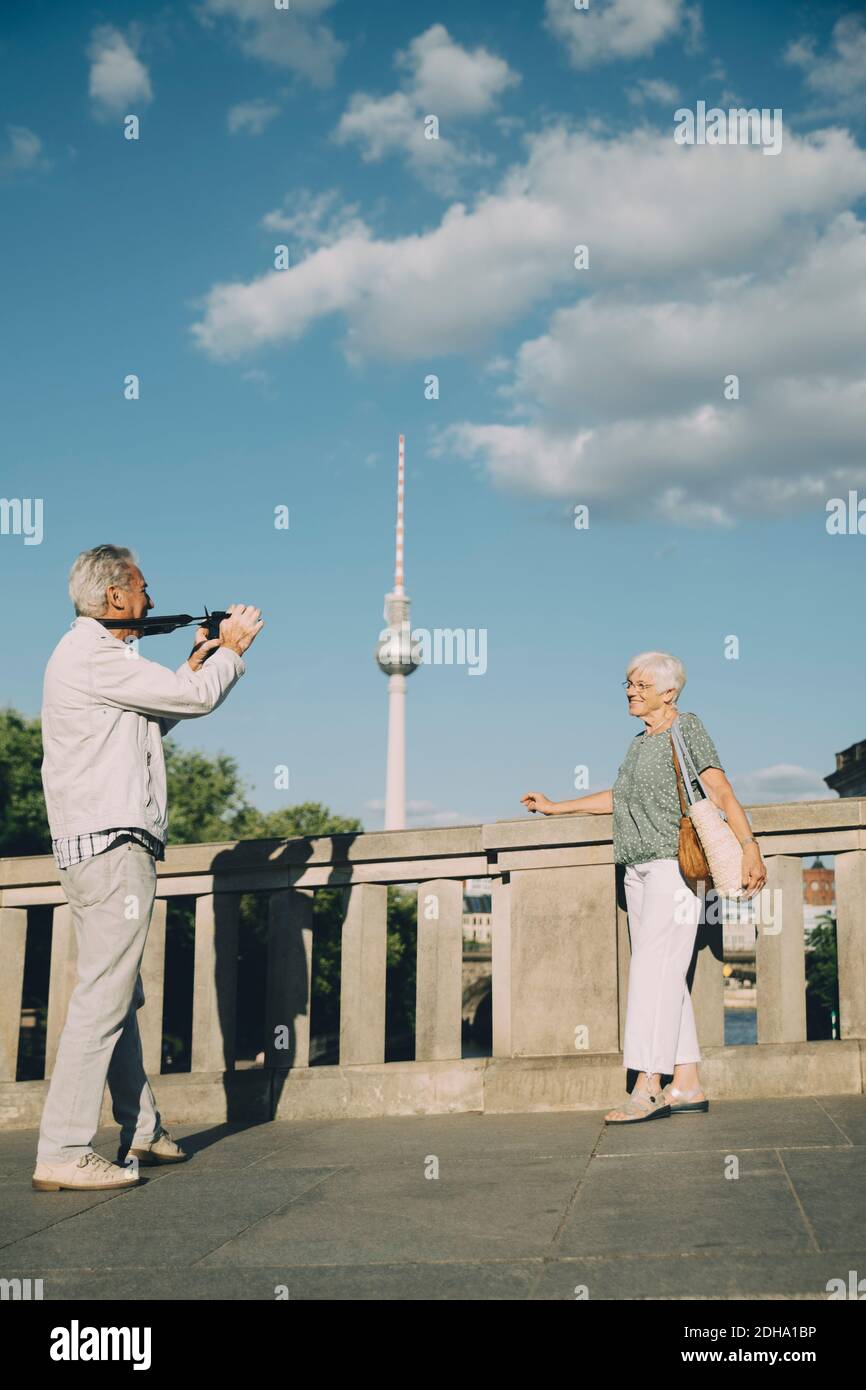 Volle Länge des Mannes fotografieren ältere Frau, während Stehen auf Brücke gegen Turm in der Stadt Stockfoto