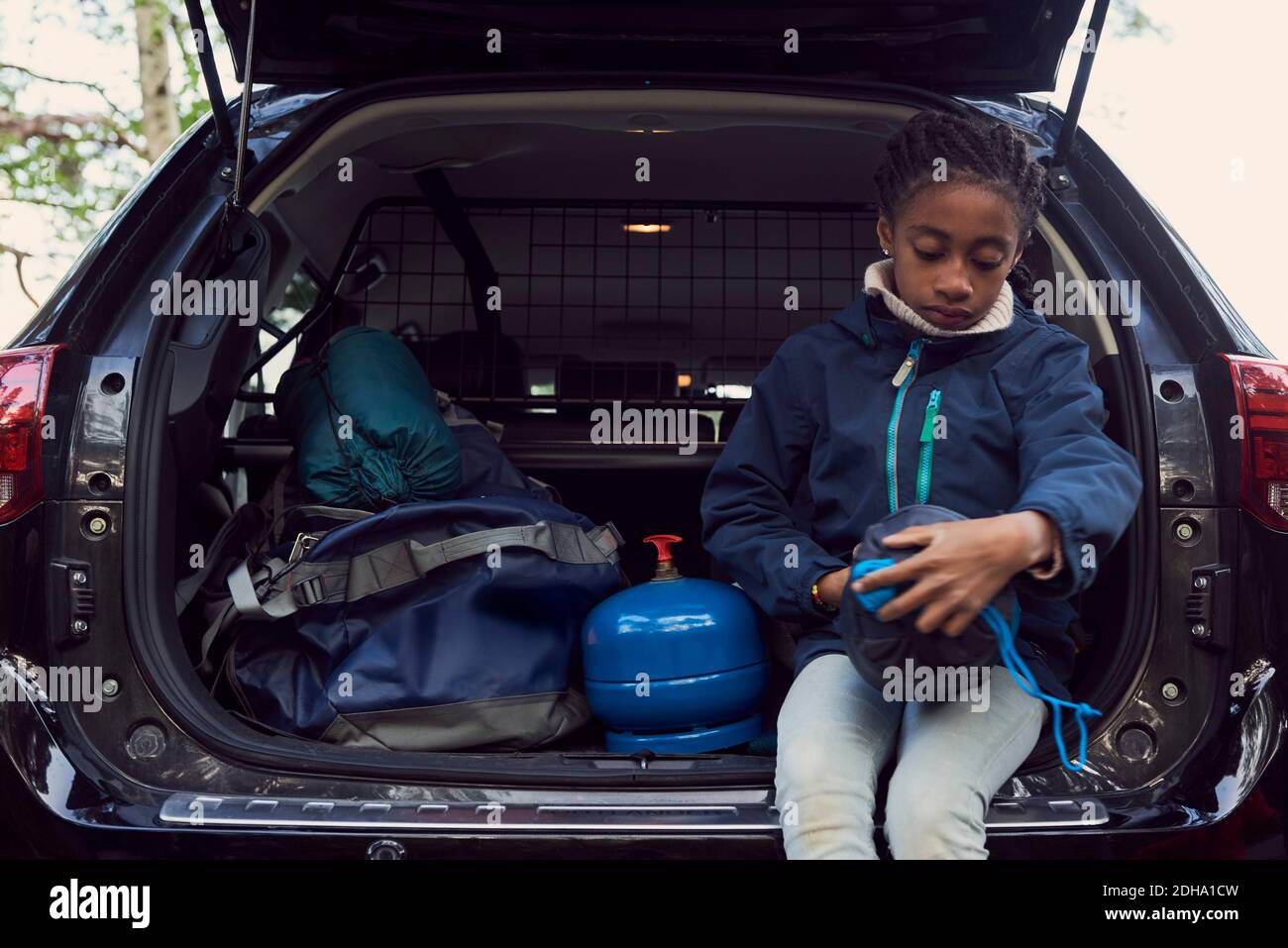 Mädchen sitzt mit Campingausrüstung im Kofferraum Stockfoto