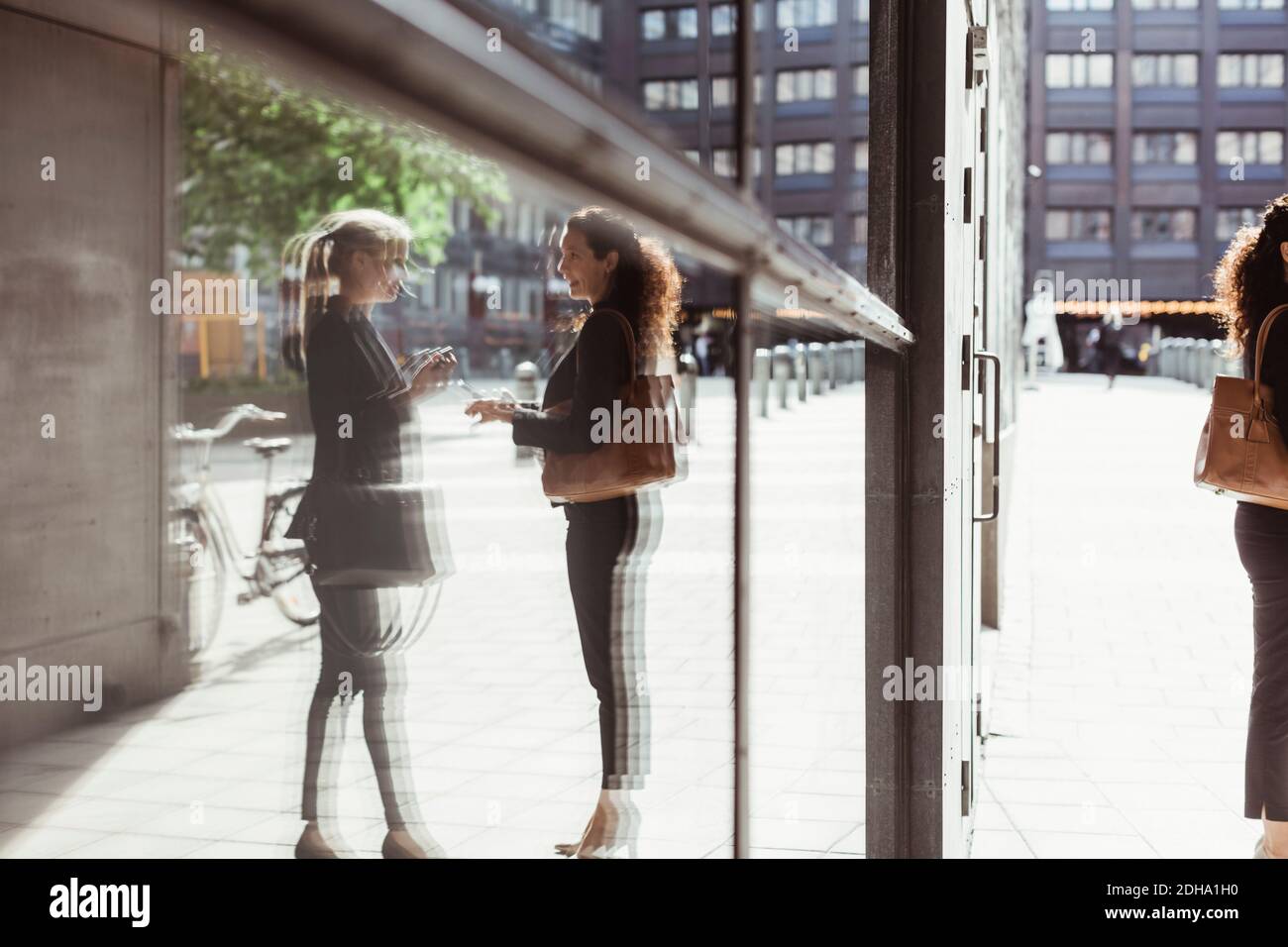 Spiegelung von Geschäftsfrauen, die auf dem Bau von Glas sprechen Stockfoto