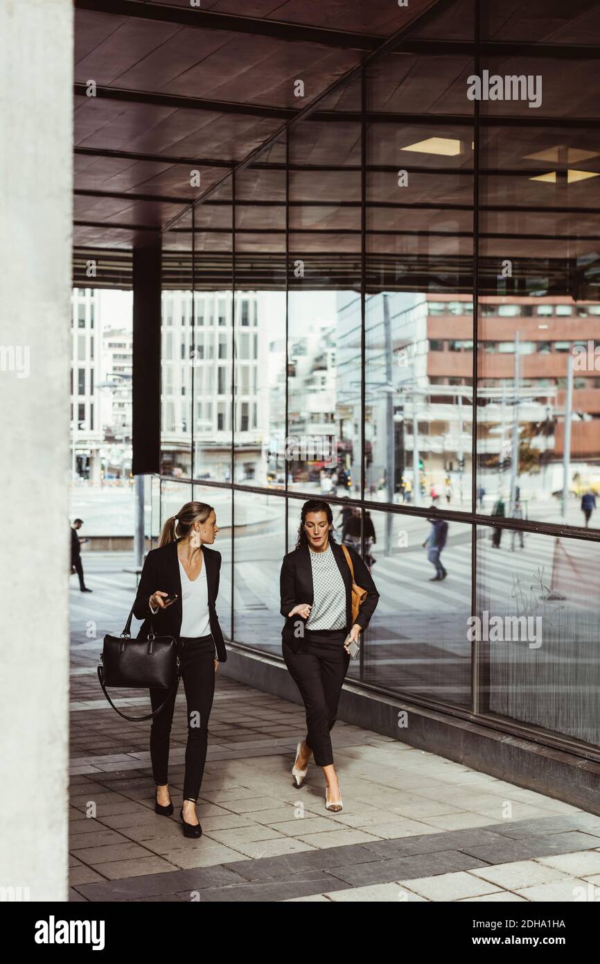 Geschäftsfrauen sprechen beim Gehen auf dem Fußweg Stockfoto