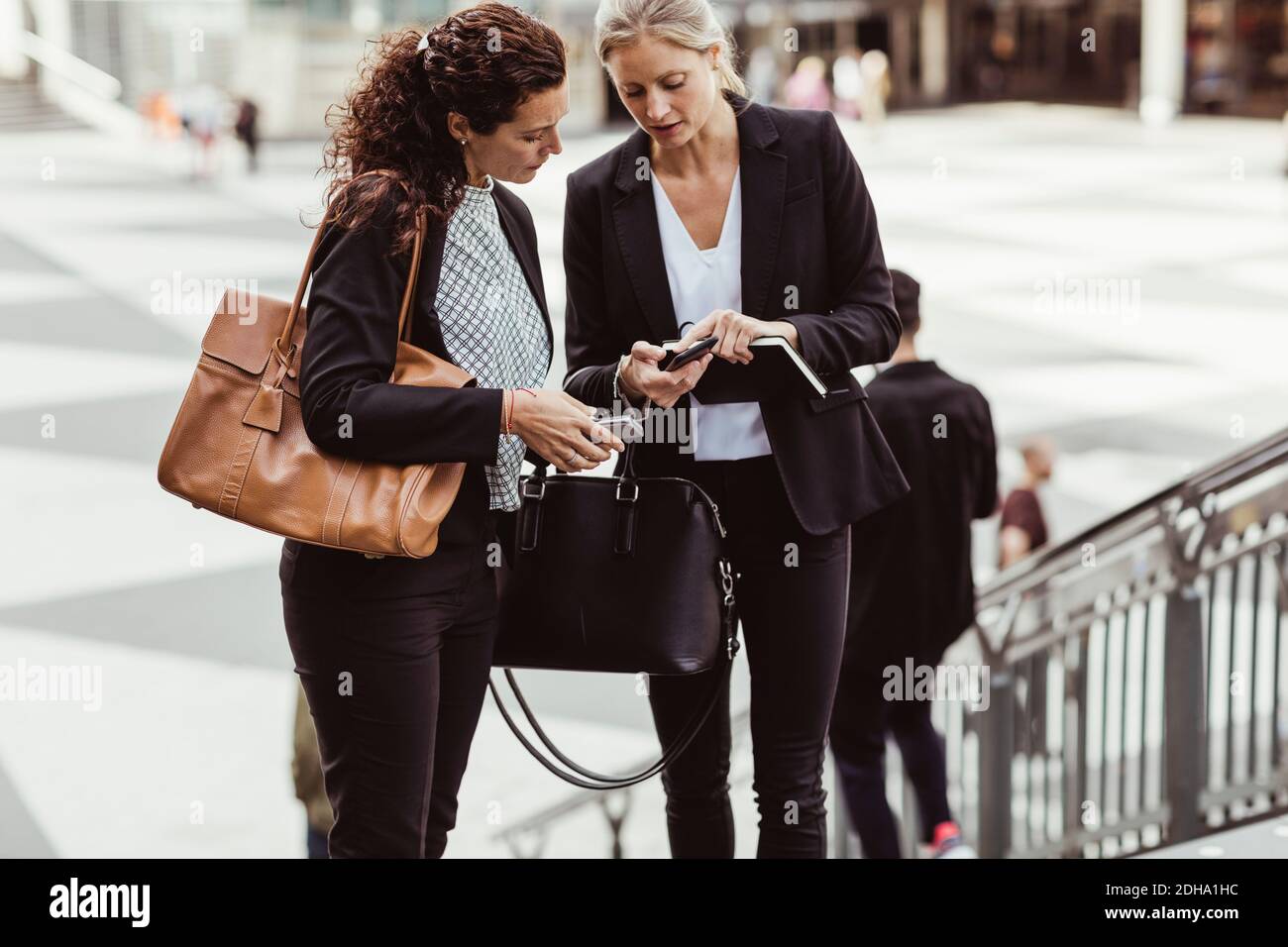 Geschäftsfrau, die einer Kollegin im Freien ein Smartphone zeigt Stockfoto