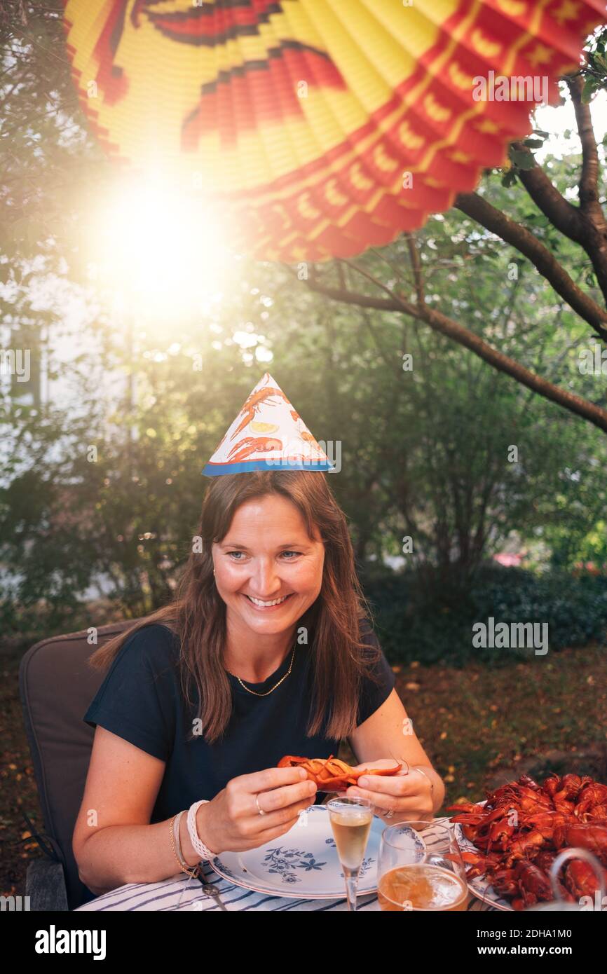 Glückliche reife Frau, die Krebse isst, während sie am Esstisch sitzt Während Gartenparty Stockfoto