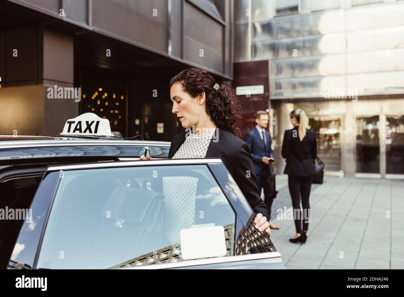 Weibliche Unternehmerin in Taxi eingeben, während Mitarbeiter im Hintergrund stehen Stockfoto