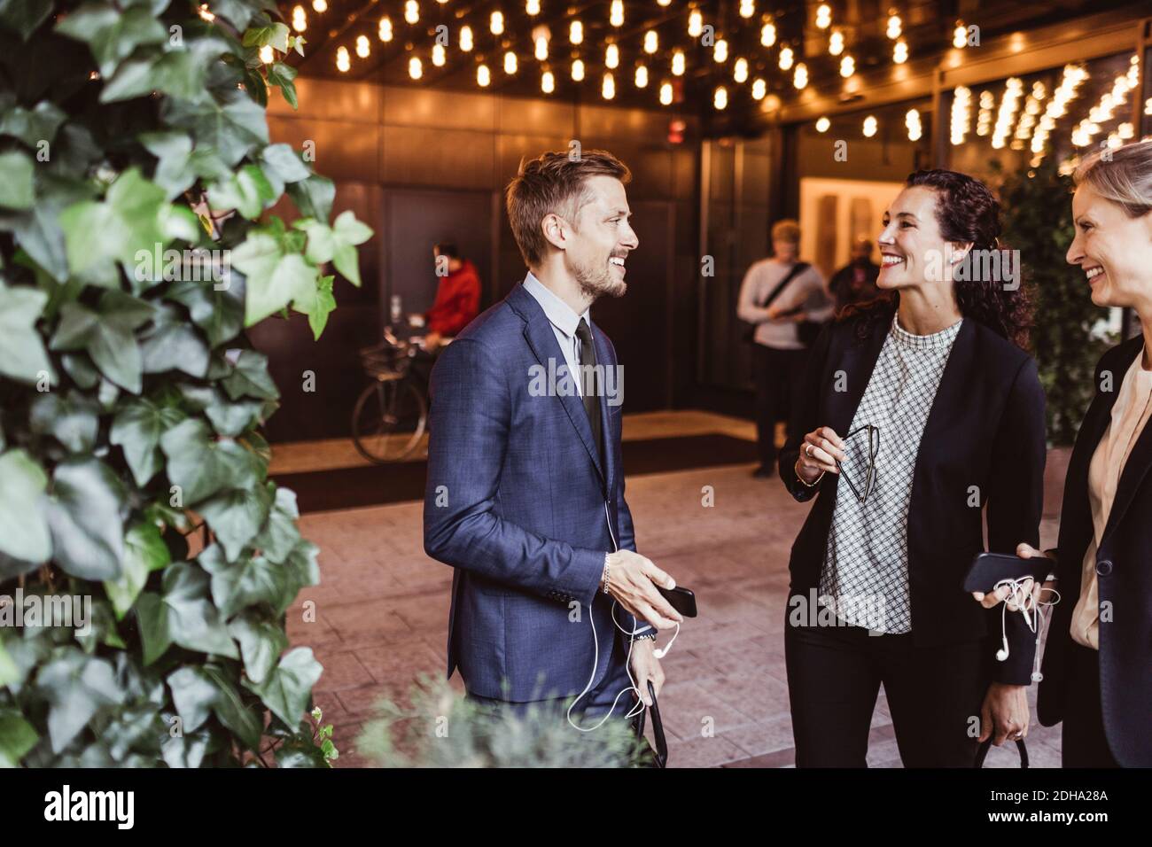 Männlicher Unternehmer lächelt mit Mitarbeitern, während er am Eingang des Gebäudes steht Stockfoto