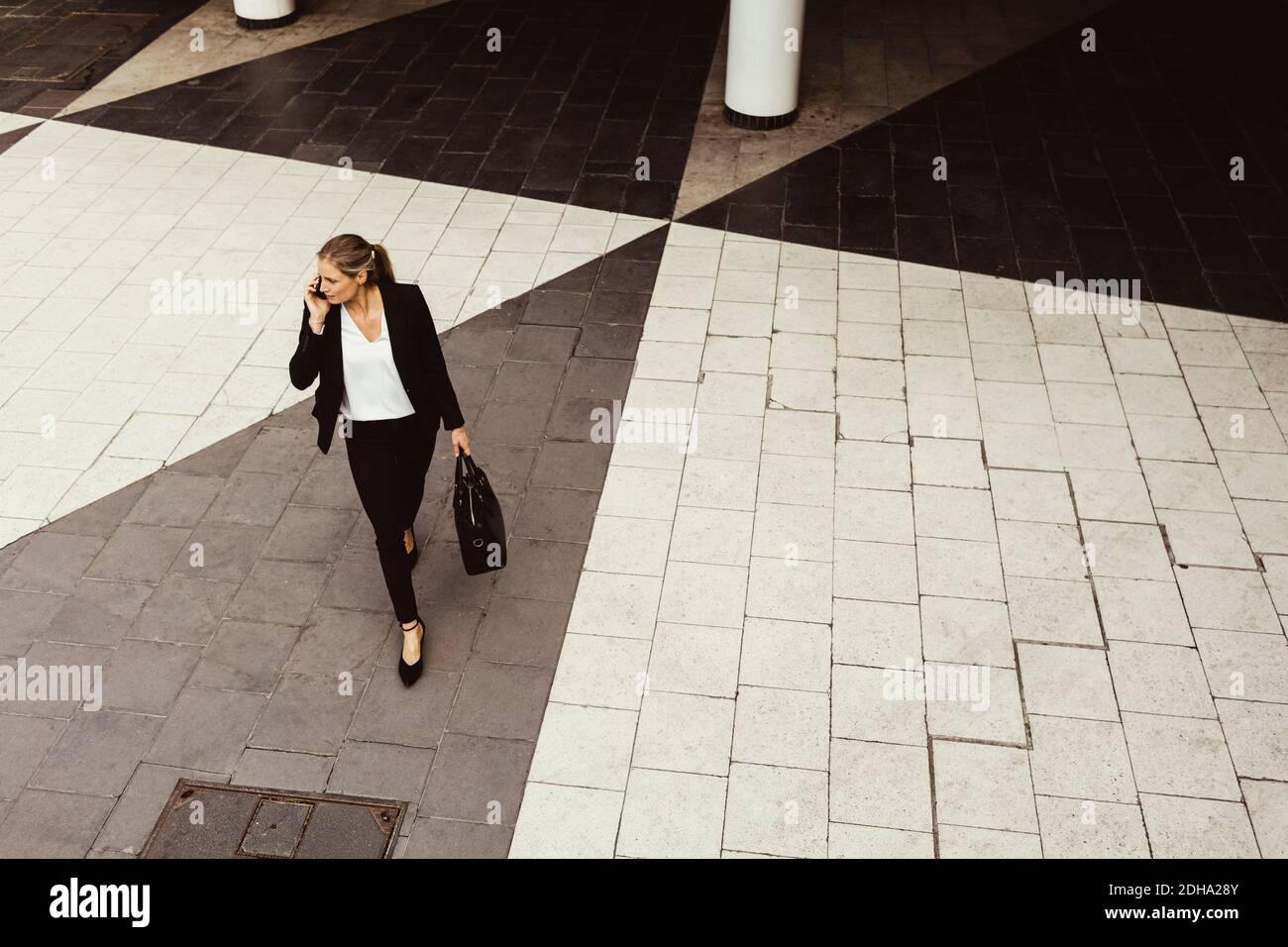 Die Geschäftsfrau, die während des Gehens telefoniert, hat einen hohen Blickwinkel Auf der Straße Stockfoto