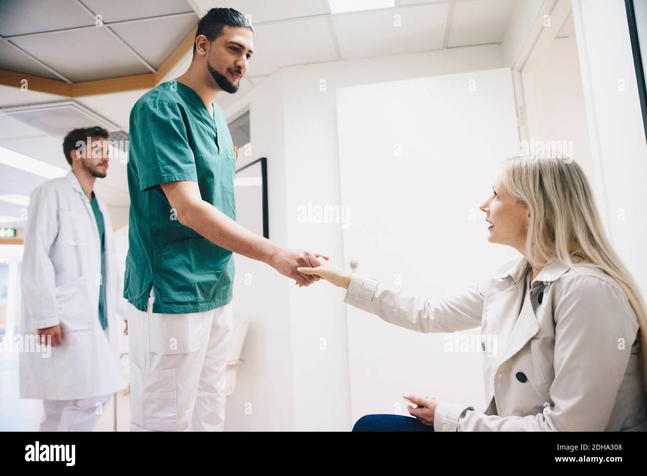 Seitenansicht der Patientin, die sich mit dem jungen Mann die Hände schüttelt Krankenschwester im Krankenhaus Stockfoto