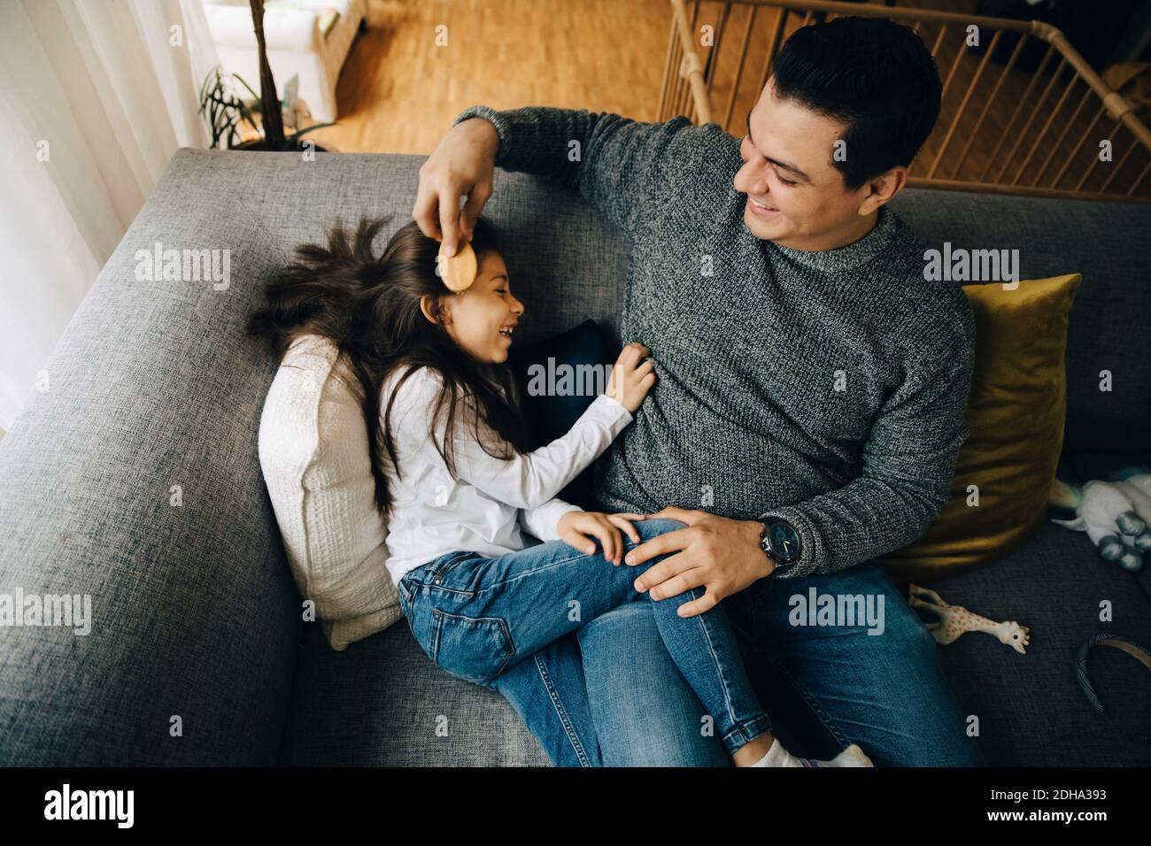 Hohe Winkelansicht des Vaters, der die Haare seiner Tochter während des Sitzens kämmt Auf dem Sofa zu Hause Stockfoto