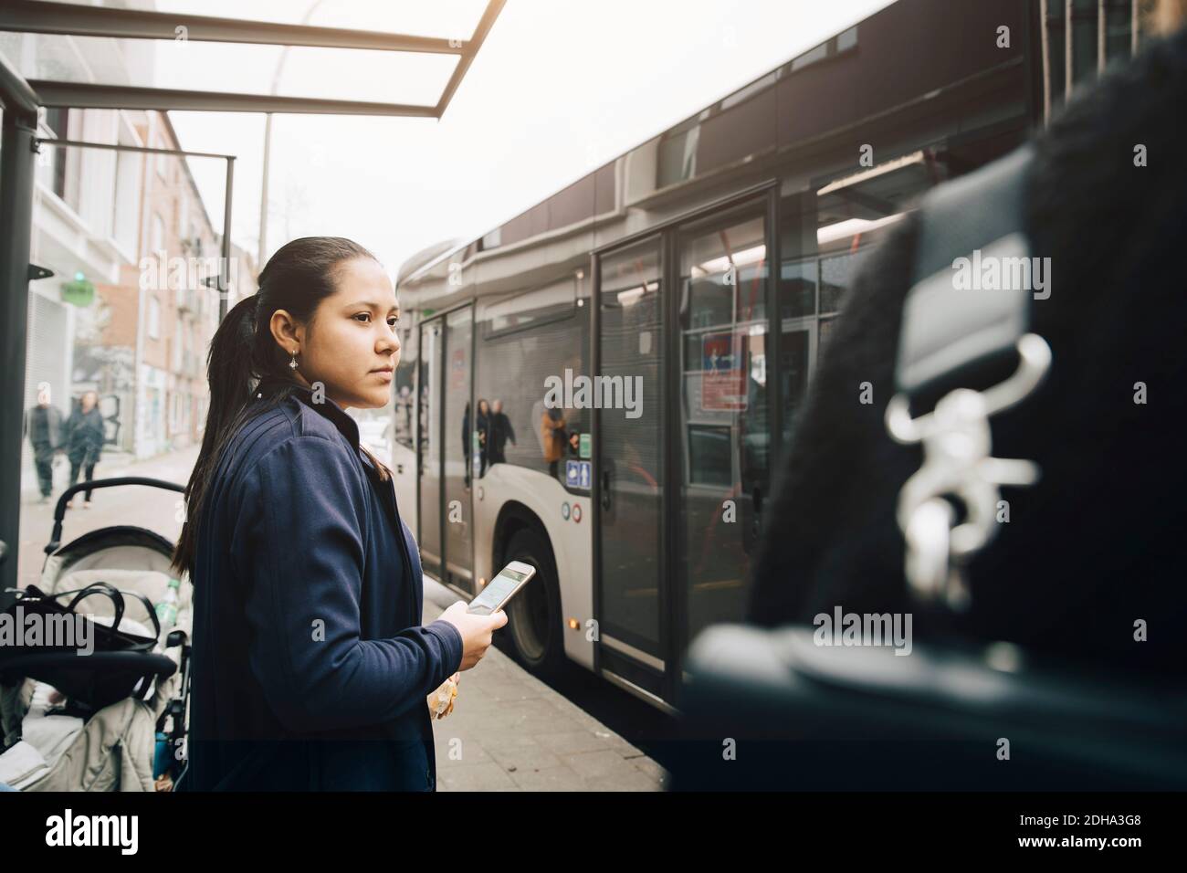 Mittlere Erwachsene Frau mit Handy, während sie auf den Bus warten In der Stadt Stockfoto