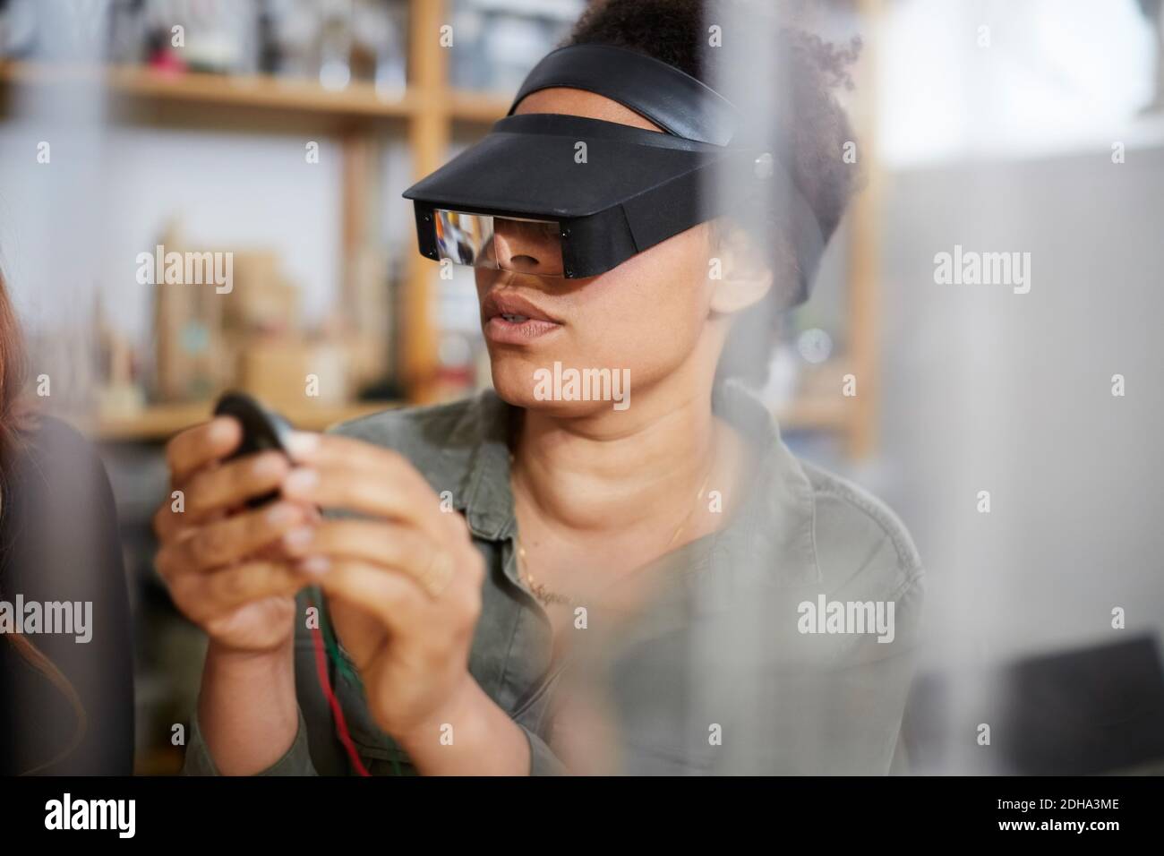 Eine Technikerin, die in der Werkstatt elektrische Bauteile durch eine Lupe betrachtet Stockfoto