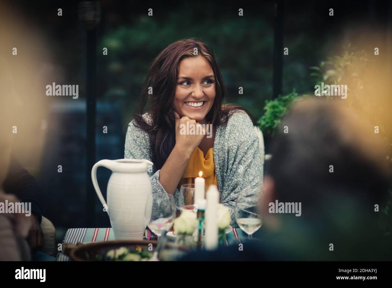 Lächelnde junge Frau, die während der Party am Esstisch sitzt Hinterhof Stockfoto