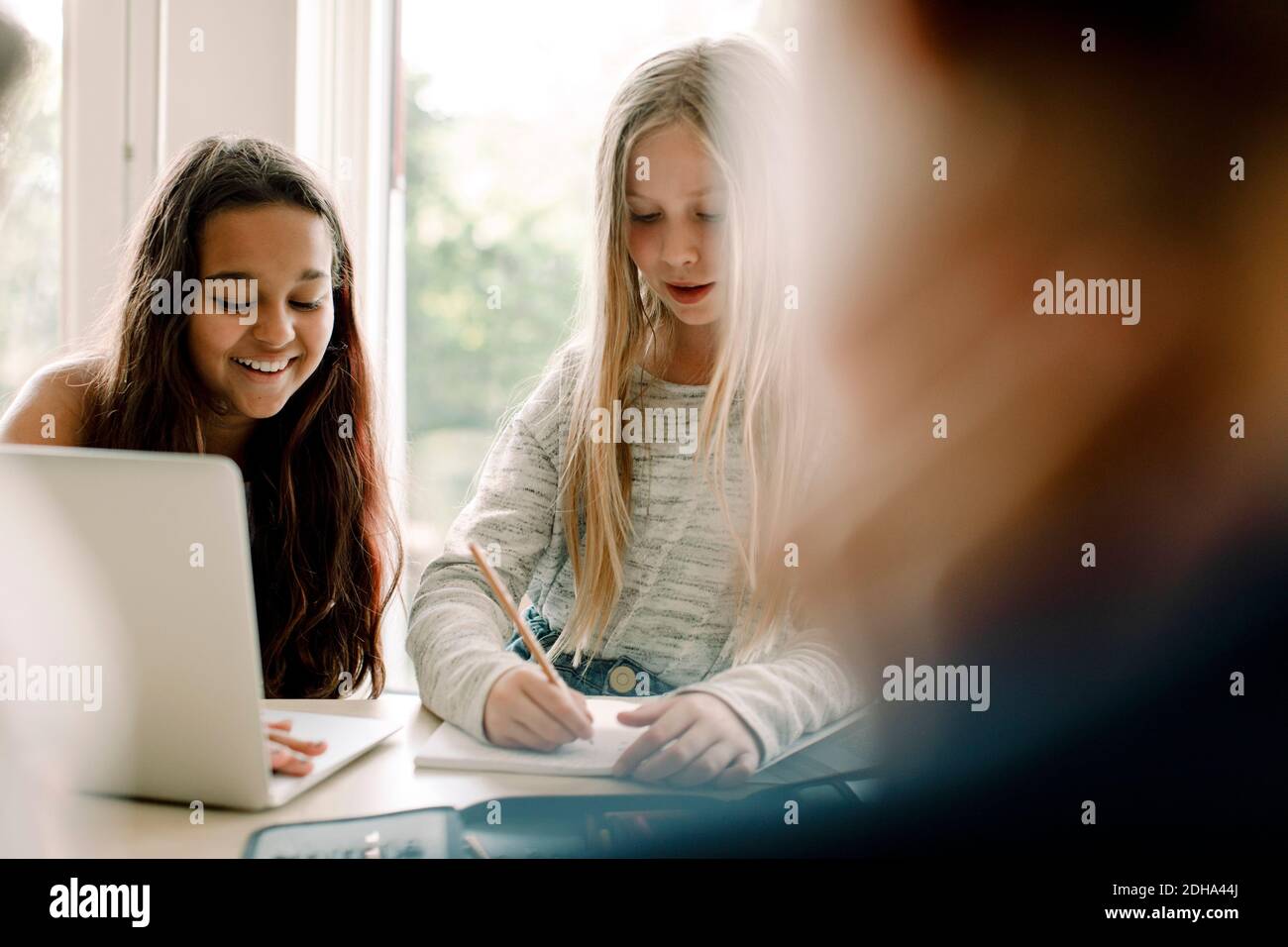 Studentin, die im Buch schreibt, während sie von einem Freund sitzt Tabelle Stockfoto