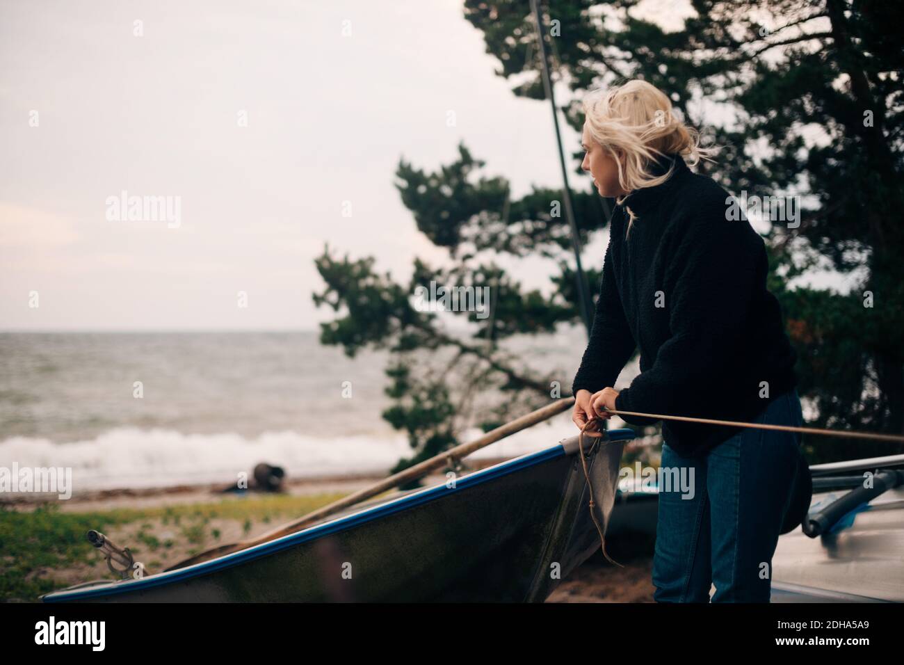 Junge Frau, die am Strand ein Boot bindet Stockfoto