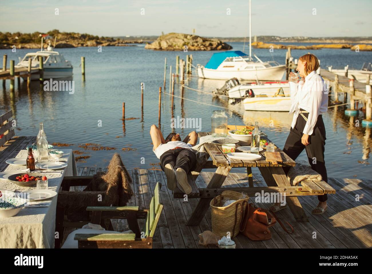 Seitenansicht einer Frau, die auf den Mann schaut, der am Hafen liegt An sonnigen Tag Stockfoto