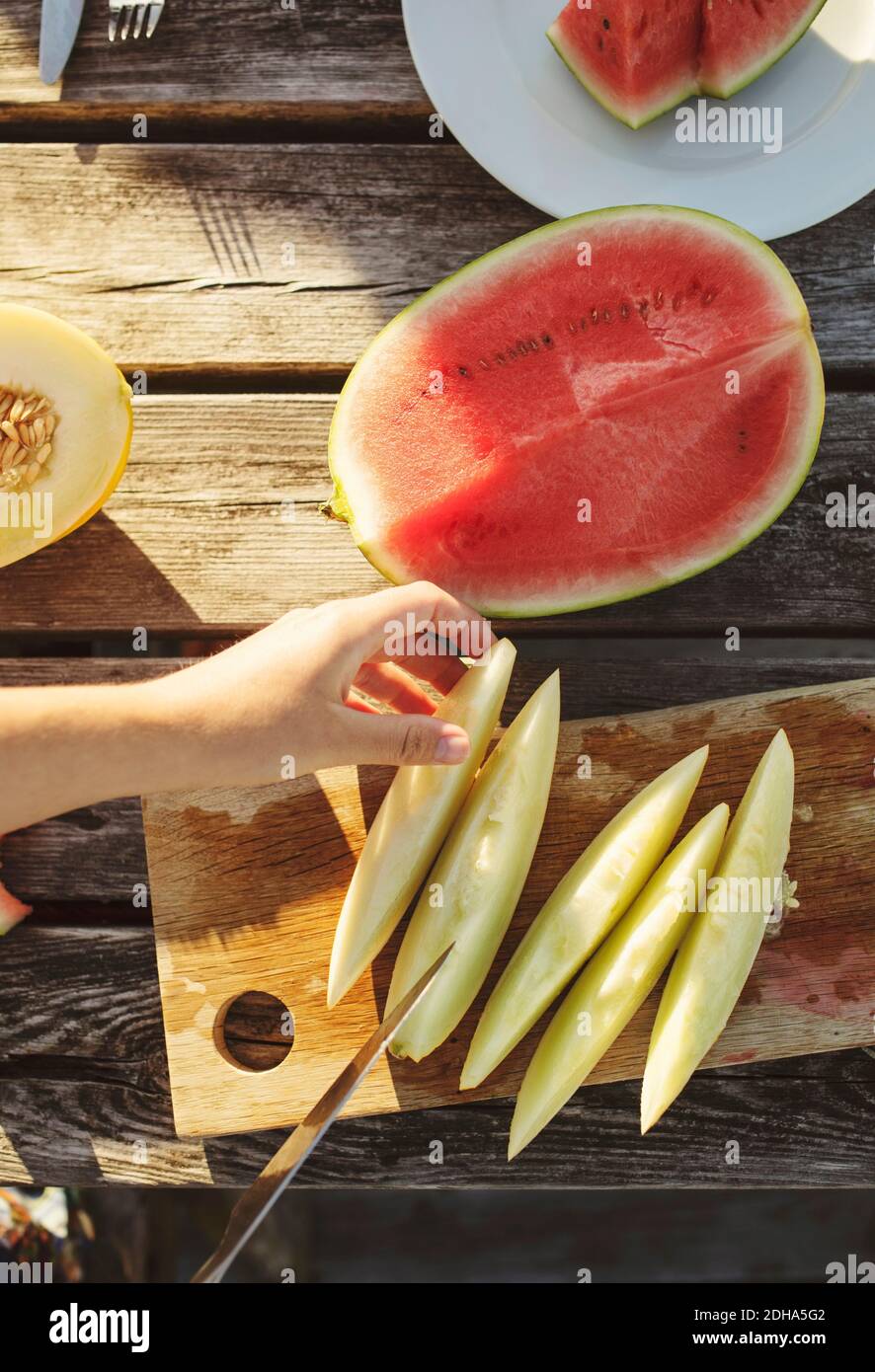 Zugeschnittenes Bild einer Frau, die Honigmelone am Tisch aufschlitzt Sonniger Tag Stockfoto