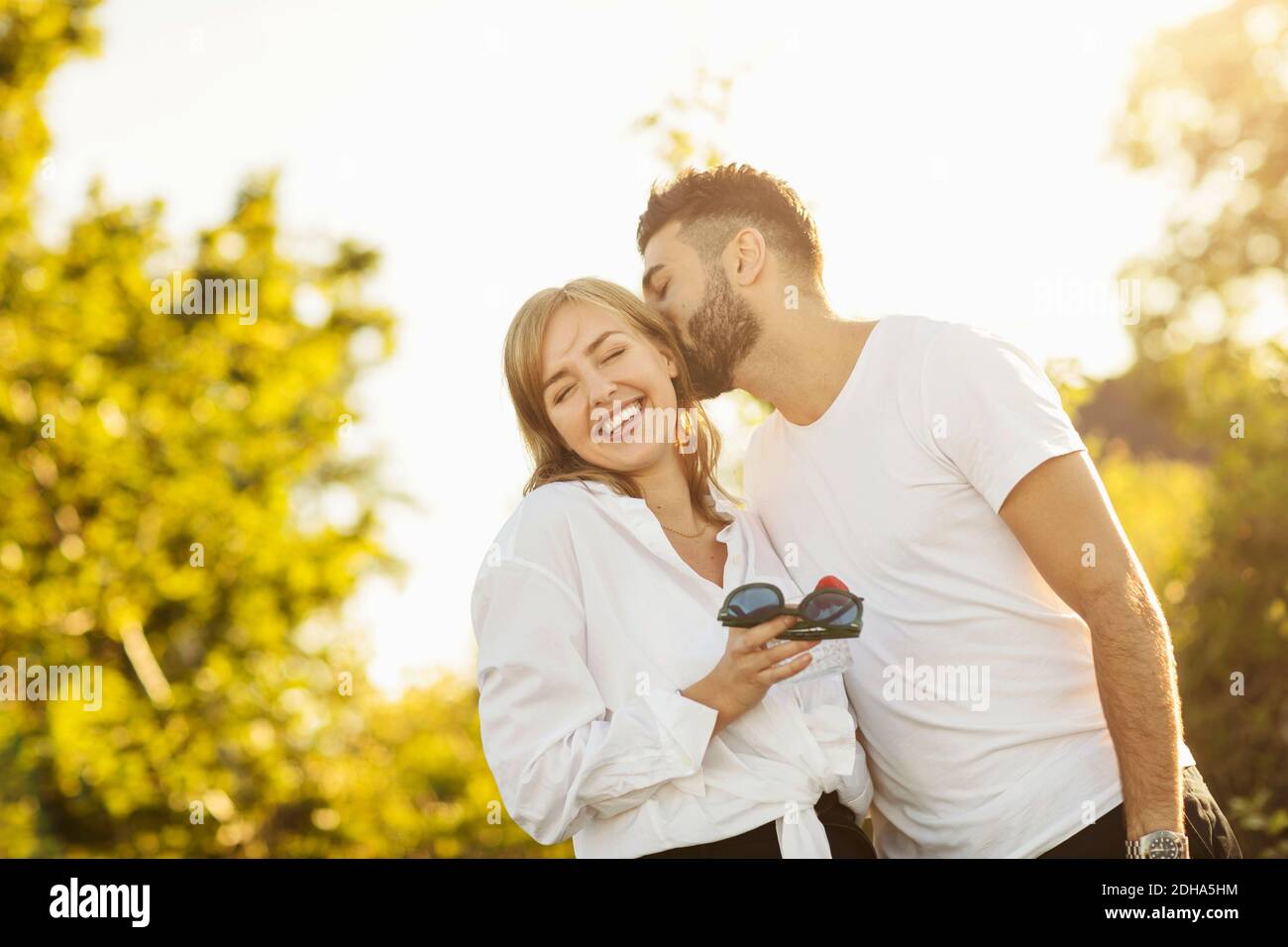 Liebevoller Mann küsst Freundin beim Stehen gegen klaren Himmel Stockfoto