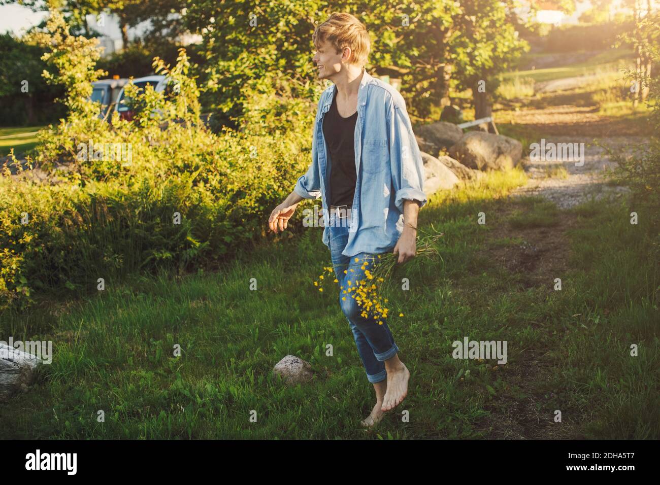 Die ganze Länge des jungen Mannes, der Blumen hält, während er weiter geht Gras Stockfoto