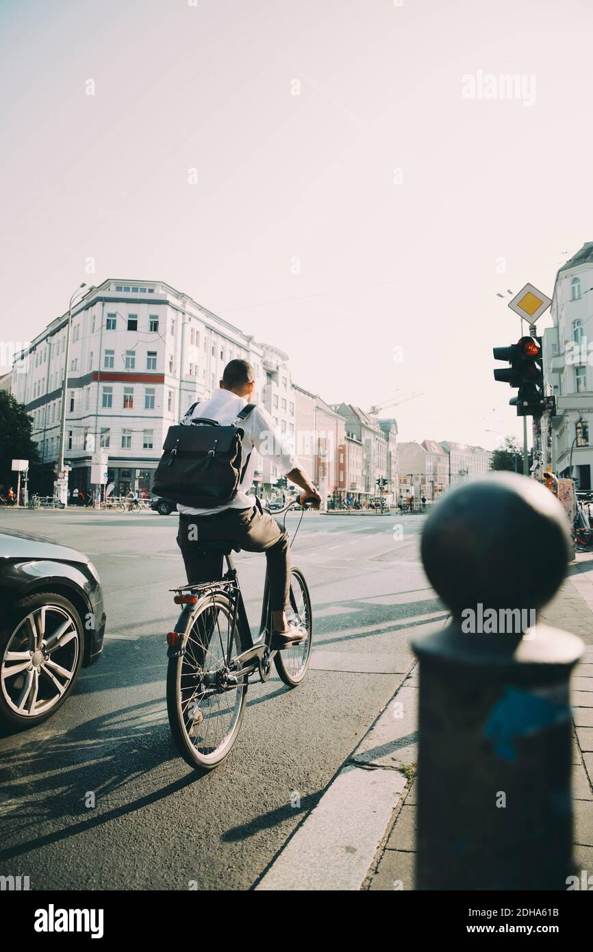 Rückansicht des Geschäftsreisenden, der auf der Straße Fahrrad fährt Stadt gegen Himmel Stockfoto