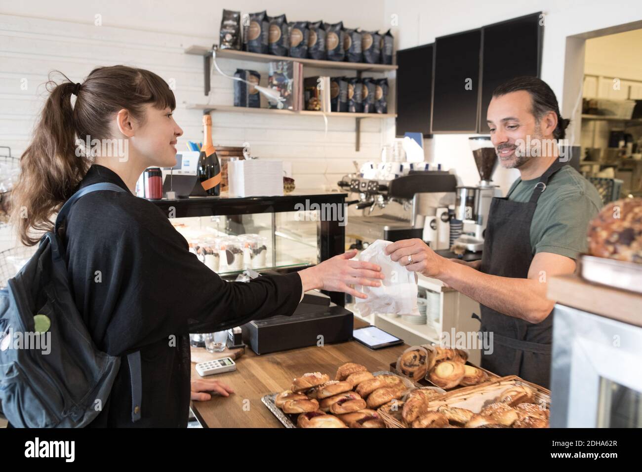 Lächelnd reifen männlichen Besitzer Serving Food-Paket für weibliche Kunden Beim Auschecken in der Bäckerei Stockfoto