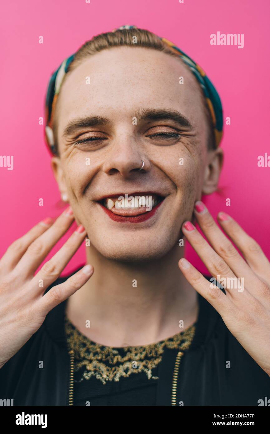 Porträt eines glücklichen jungen Mannes, der beim Gegenstehen Zunge zeigt Rosa Hintergrund Stockfoto