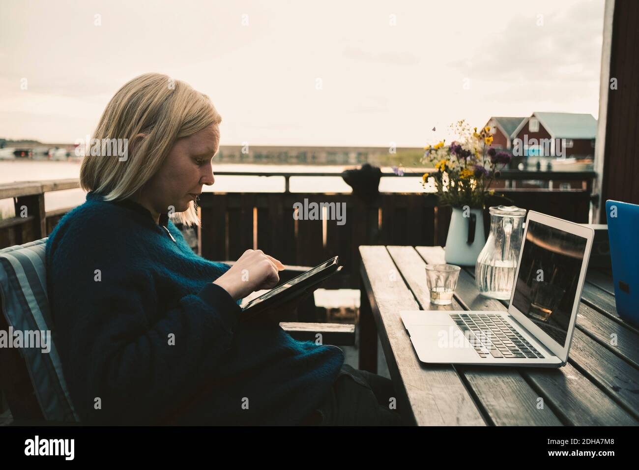 Frau mit digitalen Tablet mit Laptop auf Holztisch bei Ferienvilla Stockfoto