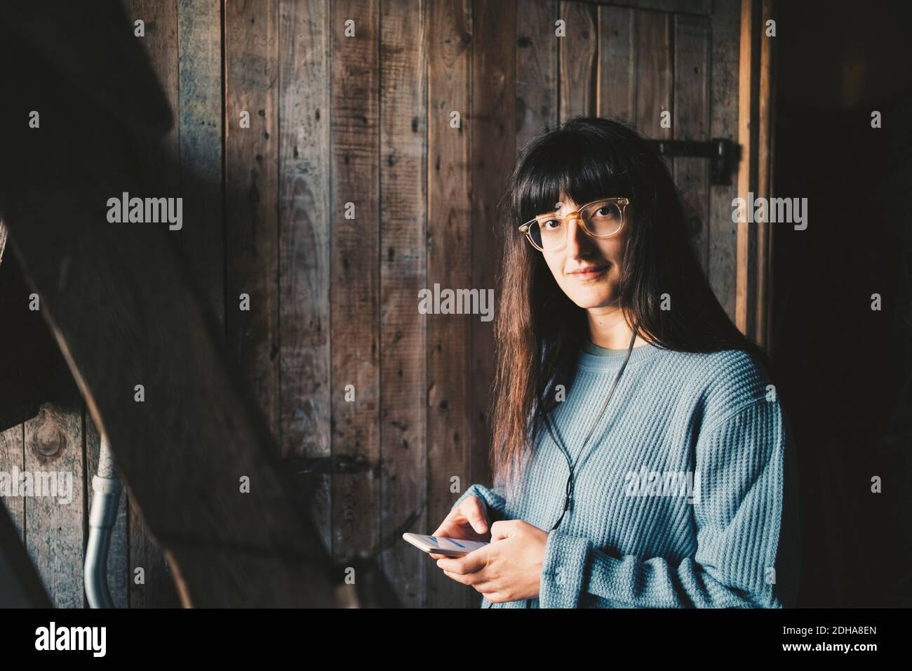 Porträt einer lächelnden Frau mit Smartphone an der Holzwand In der Ferienvilla Stockfoto