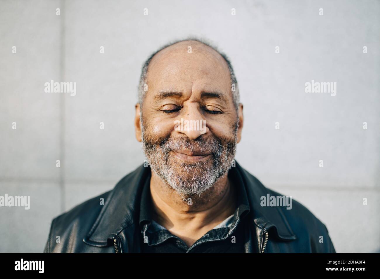 Lächelnder älterer Mann mit geschlossenen Augen gegen die Wand Stockfoto