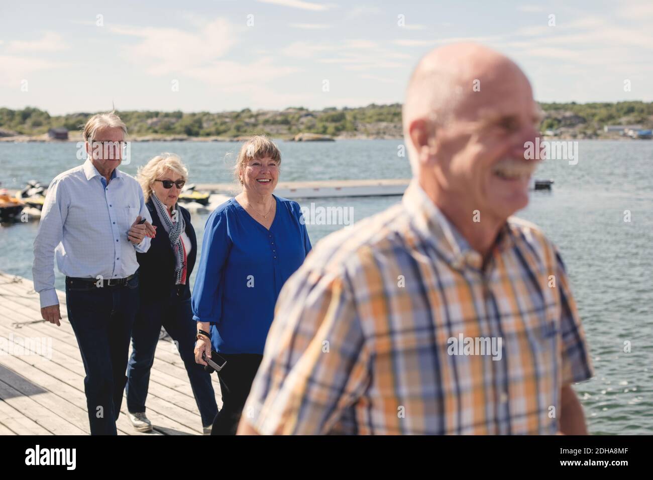 Glückliche ältere männliche und weibliche Freunde, die während des Spazierens auf dem Pier unterwegs sind Urlaub Stockfoto