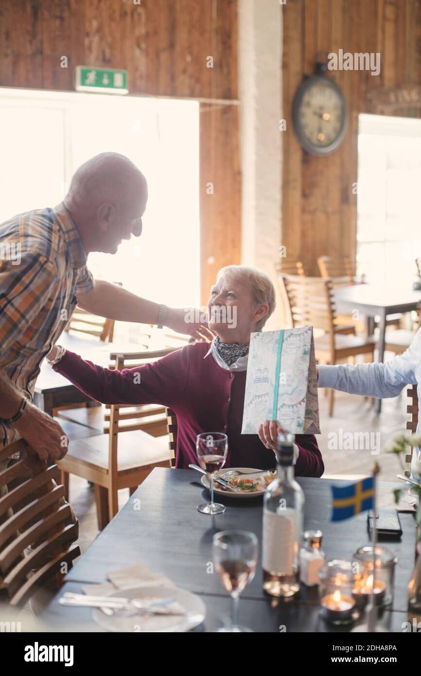 Älterer Mann im Gespräch mit einer Freundin, die am Tisch präsent hält Im Restaurant Stockfoto