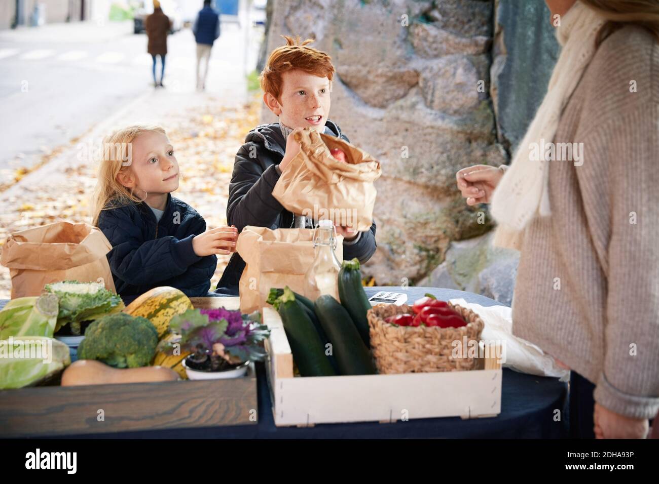 Männliche und weibliche Geschwister kaufen Gemüse von weiblichen Marktverkäufer Stockfoto