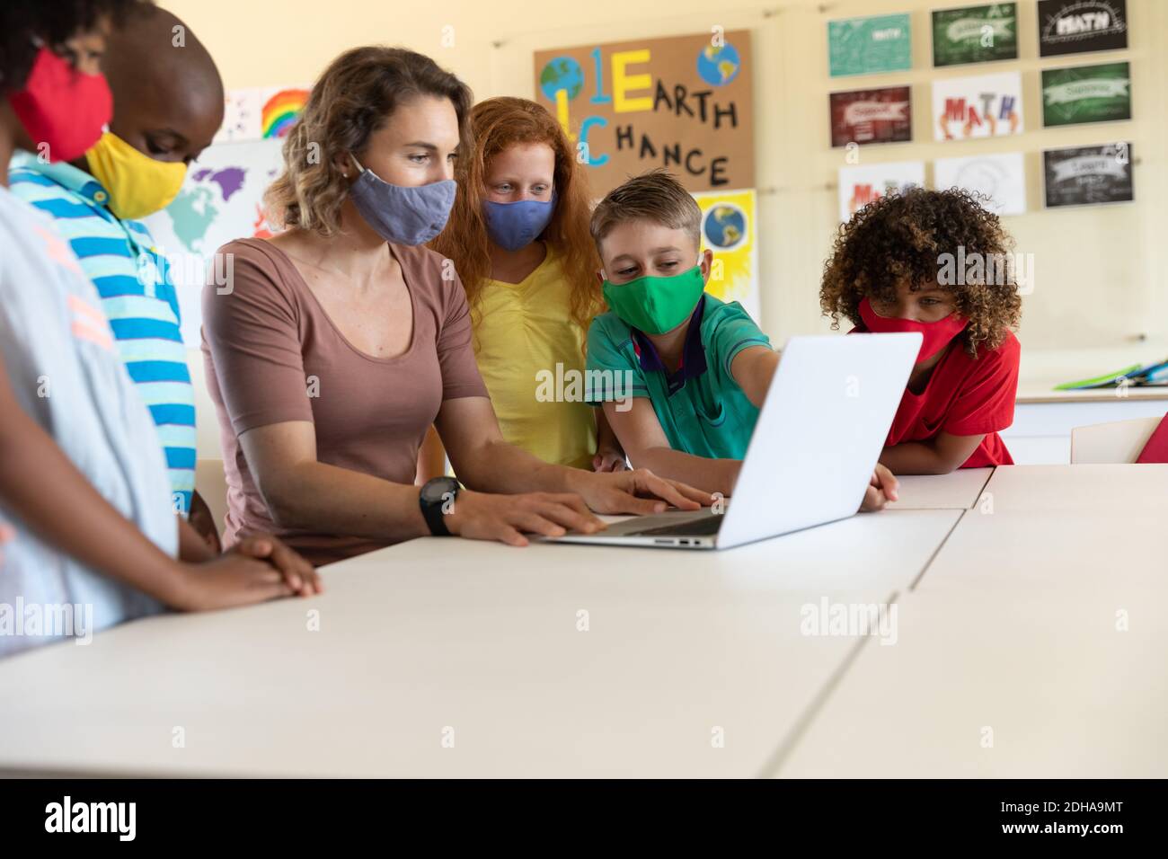 Weibliche Lehrerin trägt Gesichtsmaske mit Laptop, um Schüler zu lehren In der Klasse Stockfoto
