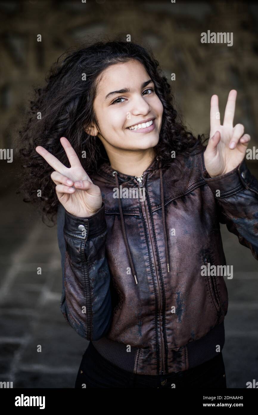 Portrait von Teenager-Mädchen mit schwarzen lockigen Haaren zeigt Frieden schild am Parkhaus Stockfoto