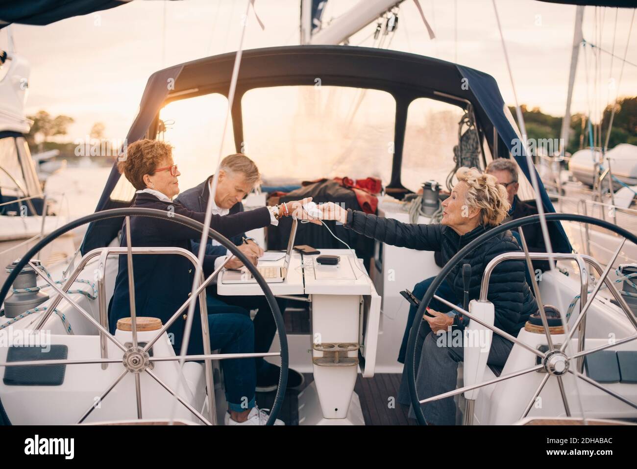 Ältere Frau, die auf Reisen das Ladegerät an eine Freundin übergibt In Yacht Stockfoto