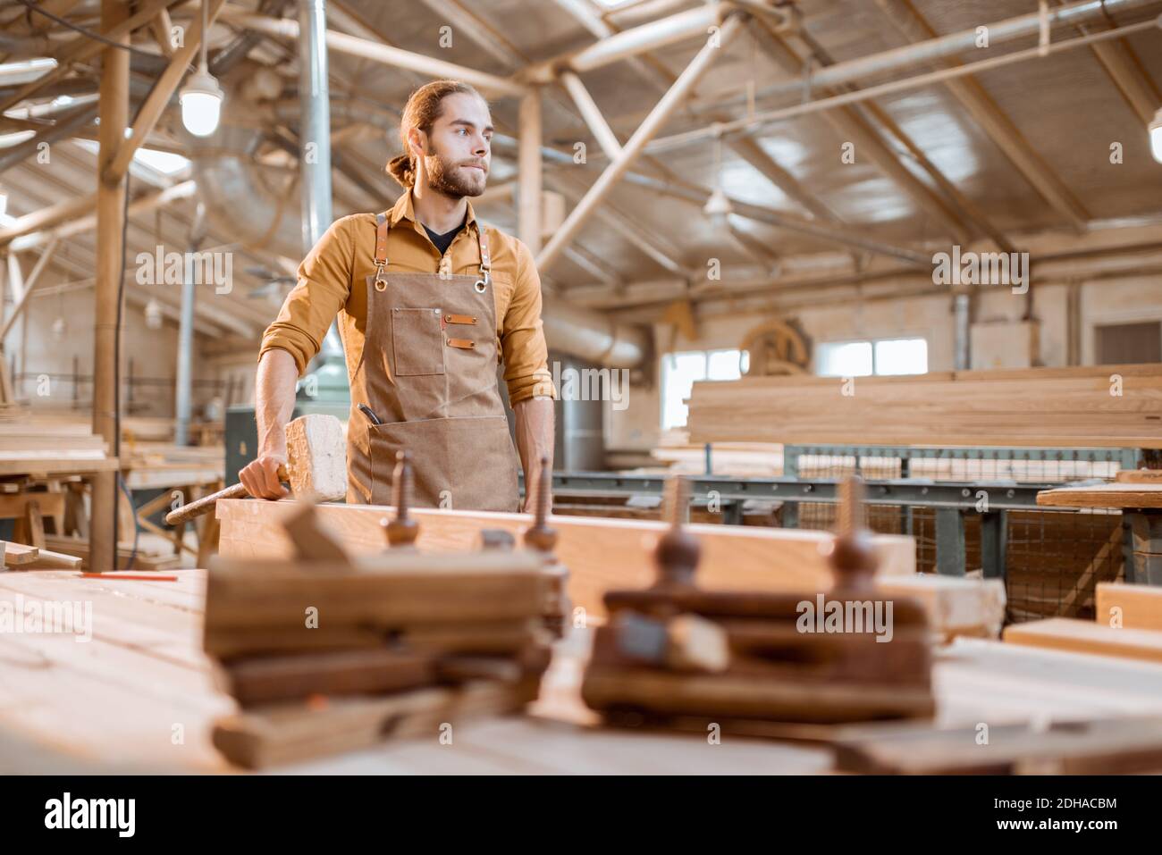 Porträt eines schönen Zimmermanns, der in der Nähe der Werkbank an der alten handwerklichen Schreinerei steht Stockfoto