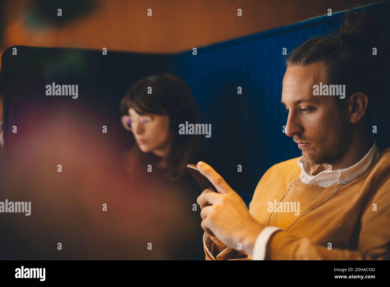 Mittelerwachsener Geschäftsmann, der Smartphone benutzt, während er bei jungen Leuten sitzt Weibliche Kollegin in der Bürokantine Stockfoto