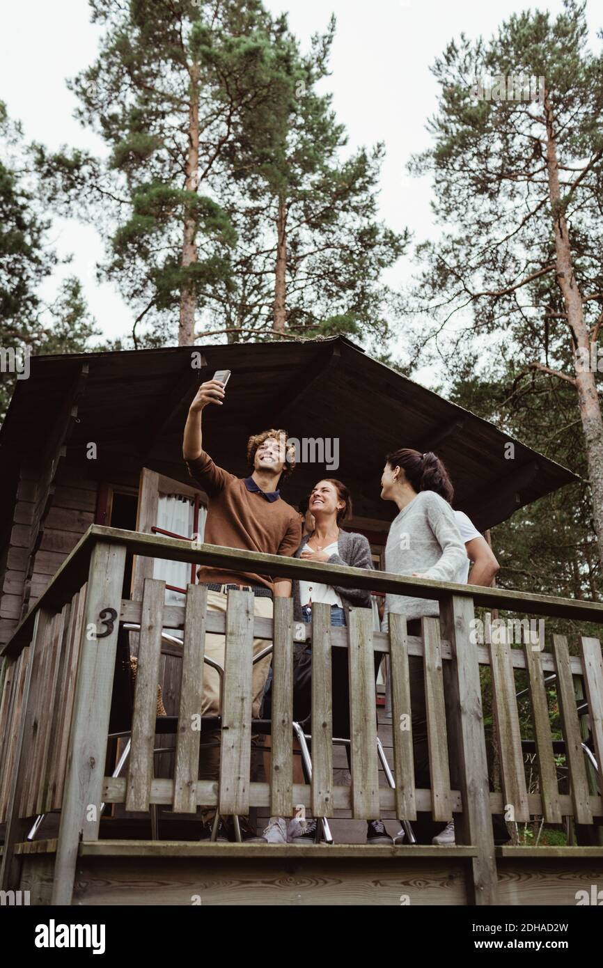 Lächelnde Freunde, die Selfie mit dem Mobiltelefon machen, während sie im Telefon stehen Veranda Stockfoto
